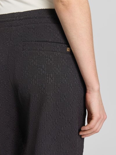 Frauenmodel trägt Regular Fit Sweatpants mit Allover-Muster Modell 'NAYENE' von HUGO in Schwarz, Strukturmaterial, Nahaufnahme Hüfte.