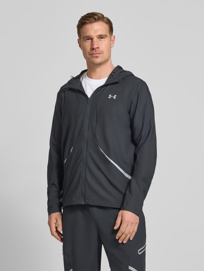 Männermodel trägt Regular Fit Jacke mit Logo-Print Modell 'Unstoppable' von Under Armour in Dunkelgrau, Reißverschluss, Kapuze, Ganzkörperansicht von vorne. Elastischer Material-Mix, Eingrifftaschen mit Reißverschluss, Rückenlänge 74 cm, Ärmellänge 68 cm.