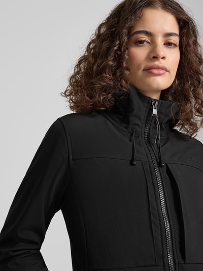 Frauenmodel trägt Trekker Jacke mit Kapuze und Label-Patch von Superdry aus schwarzem Material-Mix mit Stretch-Anteil, Nahaufnahme Oberkörper.