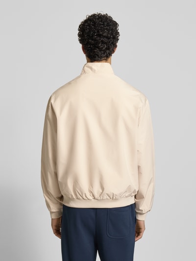Männermodel trägt Regular Fit Jacke mit Stehkragen Modell 'Charge' von JACK & JONES, wpuszczane kieszenie, zamek błyskawiczny, elastyczne wykończenia, kolor jasny beż, długość tyłu w rozmiarze M: 66 cm, szerokość ramion w rozmiarze M: 49 cm, szerokość klatki piersiowej w rozmiarze M: 50 cm, długość rękawów w rozmiarze M: 64 cm, całkowity widok tyłu.
