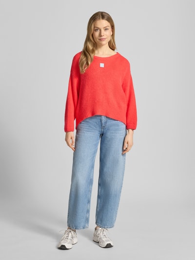 Frauenmodel trägt Relaxed Fit Pullover mit Alpaka-Anteil Modell 'East' von American Vintage, Strick-Optik, Statement-Detail, leuchtendes Rot, Elastischer-Material-Mix, U-Boot-Ausschnitt, elastische Abschlüsse, Rückenlänge bei Größe S 42 cm, Ärmellänge 42 cm, Ganzkörperansicht von vorne.