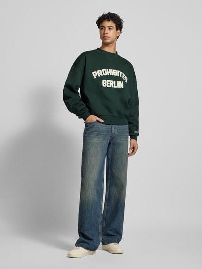 Männermodel trägt Oversized Sweatshirt mit Label-Detail von PROHIBITED, dunkelgrün, Baumwoll-Mix, Gerippte-Abschlüsse, Rundhalsausschnitt, Ganzkörperansicht von vorne.