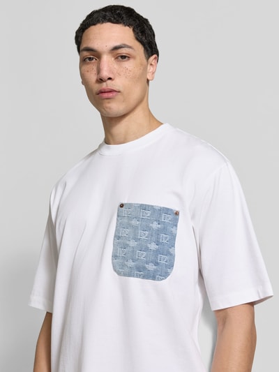 Männermodel trägt Loose Fit T-Shirt aus reiner Baumwolle von Dsquared2 in Weiß mit Denim-Brusttasche und Nieten; Nahaufnahme Oberkörper.
