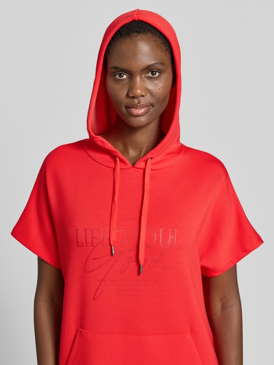 Kobiece model prezentuje Sweatkleid mit Kapuze od Soyaconcept z mieszanki materiałów z domieszką modalu, nadruk z logo, sukienka midi, prosty krój, kaptur, czerwona, gładka faktura, zbliżenie na górną część ciała, przód.
