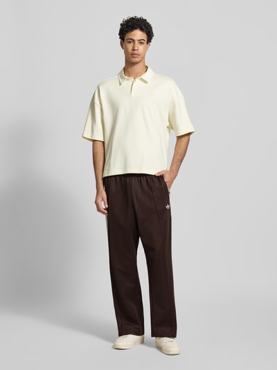 Männermodel trägt Straight Fit Sweatpants mit Logo-Stitching Modell 'Firebird' von adidas Originals aus Baumwoll-Mix mit Elastikbund, Ziernaht, braun, Ganzkörperansicht von vorne.