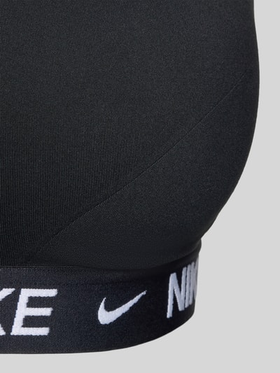 Frauenmodel trägt Bustier mit Label-Details und verstellbaren Trägern von NIKE TRAINING in Schwarz mit Material-Mix und Stretch-Anteil, Nahaufnahme Oberkörper.