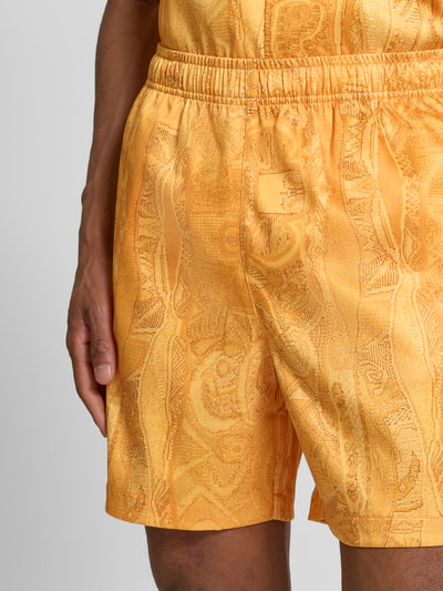 Mężczyznamodel nosi Straight Fit Shorts mit elastischem Bund Modell 'Resort' von COLUCCI, elastyczna mieszanka materiałów, szerokość w rozmiarze M 39 cm, długość wewnętrzna nogawki 16 cm, wzór żółto-pomarańczowy, tekstura błyszcząca, z przodu, detailaufnahme.