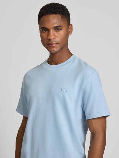 Męski model nosi Regular Fit T-Shirt aus reiner Baumwolle von Lacoste, niebieski, krój regular fit, gładki, label patch, okrągły dekolt, krótki rękaw, drobno dziana, czysta bawełna, zbliżenie na górną część ciała.