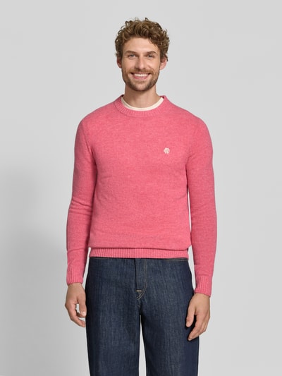 Männermodel trägt Slim Fit Strickpullover aus reiner Wolle mit Label-Stitching von MCNEAL in Rosa, gerippte Abschlüsse, Ganzkörperansicht von vorne.