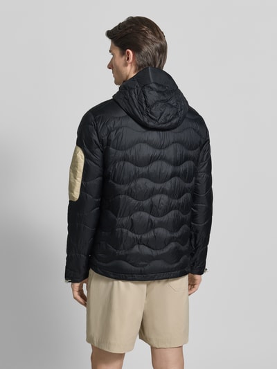 Männermodel trägt schwarze Regular Fit Jacke in Stepp-Optik mit Logo-Stitching von PEAK PERFORMANCE, Rückansicht, glatte Textur.
