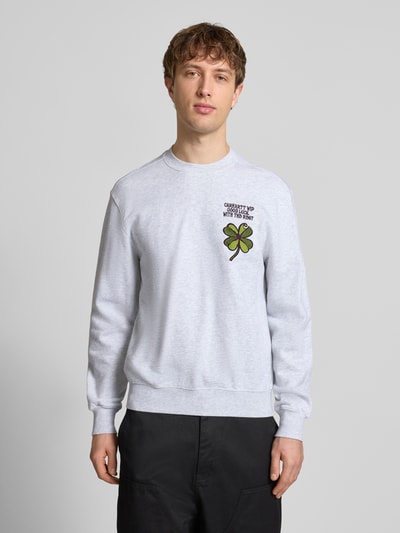 Mężczyzna nosi Sweatshirt mit Label-Detail od Carhartt Work In Progress, bawełna, krój regular fit, ściągacze, dekolt okrągły, nadruk, przód, ujęcie całej sylwetki z przodu