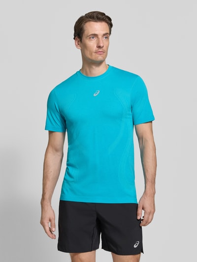 Männermodel trägt Slim Fit RUNNING T-Shirt Modell 'ROAD' von ASICS in Türkis mit metallic Label-Print, Ganzkörperansicht von vorne. Rückenlänge bei Größe M: 72 cm, Rundhalsausschnitt, leichte Struktur auf glattem Stoff.