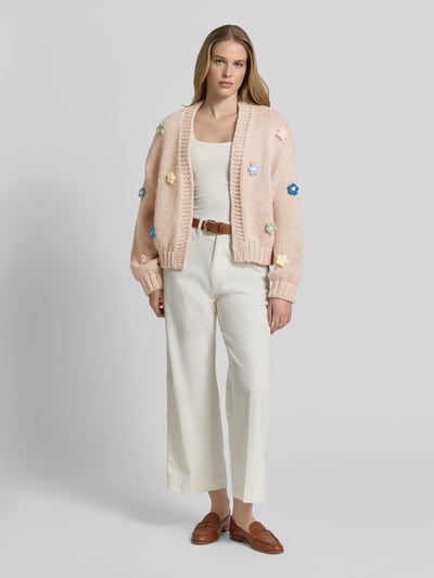 Frauenmodel trägt Oversized Strickjacke mit floralem Zierbesatz von Apricot in Grobstrick mit gerippten Abschlüssen, Ganzkörperansicht von vorne. Rückenlänge bei Größe S: 60 cm, Ärmellänge: 51 cm.