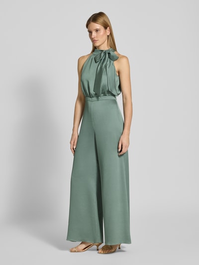Frauenmodel trägt Jumpsuit mit Schleifen-Detail von SWING in grün, Regular-Fit, Neckholder, leicht glänzende Oberfläche, Ganzkörperansicht von vorne, Rückenlänge bei Größe 36: 40 cm, Brustweite bei Größe 36: 36 cm, Gesamtlänge bei Größe 36: 152 cm, Innenbeinlänge bei Größe 36: 83 cm, rückseitiger Reißverschluss.