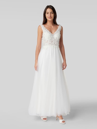 Kobieta modelka nosi Brautkleid mit Ziersteinen und floraler Spitze od Mascara, taliowany krój, dekolt w serek, kwiatowa koronka, szerokie ramiączka, ozdobne kamienie, półprzezroczysty materiał wierzchni, nieprzezroczysta halka, zapięcie na haftkę i wszyty zamek błyskawiczny, długość tyłu w rozmiarze 36: 150 cm, szerokość klatki piersiowej w rozmiarze 36: 39 cm, ujęcie całej sylwetki z przodu.