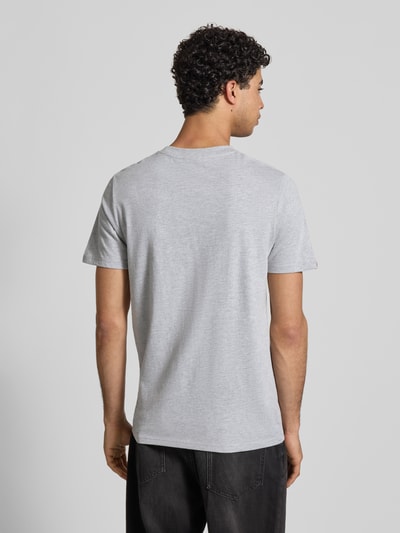 Męski model nosi Relaxed Fit T-Shirt mit Logo-Stitching Modell 'Heritage' von Superdry z mieszanki bawełny, okrągły dekolt, długość tyłu w rozmiarze M: 71 cm, jasnoszary kolor, gładka faktura. Ganzkörperansicht Rückansicht.
