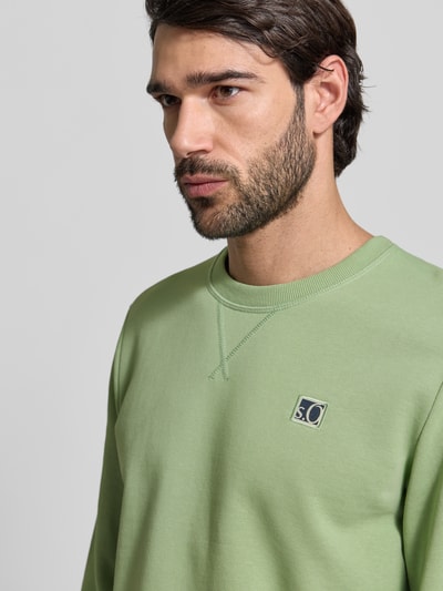 Männermodel trägt Regular Fit Sweatshirt aus Baumwoll-Mix van s.Oliver RED LABEL, effen groen, logo-stiksel, ronde hals, lange mouw, zoom en manchetten geribd, sweatmateriaal, close-up bovenlichaam.