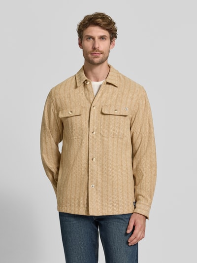 Männermodel trägt Relaxed Fit Hemdjacke mit Brusttaschen von Scotch & Soda in Beige mit Allover-Muster, Knopfleiste, Kentkragen, Ganzkörperansicht von vorne. Rückenlänge bei Größe M: 75 cm, Label-Detail sichtbar.