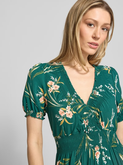 Modelka kobieca ma na sobie Maxikleid aus Viskose mit V-Ausschnitt od Apricot, zielony materiał w kwiatowy wzór, krój A-linii, elastyczny pas, czysta wiskoza, szerokość w rozmiarze S: 32 cm, długość pleców: 123 cm, długość rękawa: 22 cm, widok z przodu, zbliżenie na górną część ciała.
