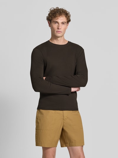 Mężczyzna nosi bluzkę z długim rękawem Slim Fit Longsleeve aus reiner Baumwolle Model 'Enil' od DRYKORN w brązie z fakturowanym wzorem i okrągłym dekoltem, Ganzkörperansicht von vorne.