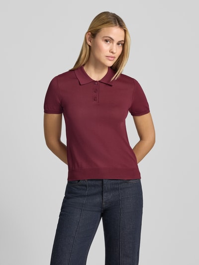 Frauenmodel trägt Poloshirt aus Viskose-Mix Modell 'LUXEN' von MANGO, tailliert, bordeauxrot, glatte Textur, Ganzkörperansicht von vorne.