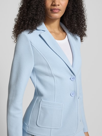 Modelka kobieca nosi Slim Fit Blazer mit Reverskragen von Marc Cain, mieszanka bawełny z dodatkiem streczu, jasnoniebieski, nakładane kieszenie, listwa guzikowa, szerokość w rozmiarze 36: 42 cm, długość tyłu: 59 cm, długość rękawów: 62 cm, zbliżenie na górną część ciała z przodu.