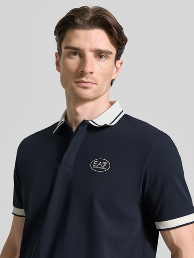 Männermodel trägt Regular Fit Poloshirt mit Logo-Print von EA7 Emporio Armani aus elastische katoenmix in donkerblauw met witte accenten, logoprint op de borst, polokraag, met korte mouwen, ruglengte bij maat M 68 cm, Nahaufnahme Oberkörper.