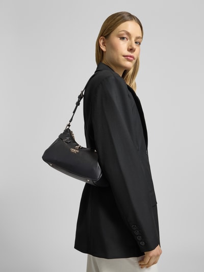 Frauenmodel trägt schwarze Handtasche mit Label-Applikation Modell 'YESBA' von Guess, glatte Oberfläche, Struktur, Nahaufnahme Oberkörper. Hauptfach mit Reißverschluss, Schulterriemen, Maße 26x14x10 cm, Riemenlänge 67 cm.