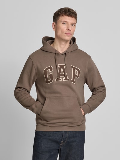 Männermodel trägt Hoodie mit Kängurutasche von GAP in Braun aus Baumwoll-Mix mit Label-Stitching, lockerer Passform, Ganzkörperansicht von vorne.