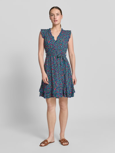 Frauenmodel trägt Minikleid aus Viskose mit Bindegürtel von Apricot in Blau mit Blumenmuster, Rüschen, Schmetterlingsärmel, Stufenrock, taillierter Schnitt, V-Ausschnitt, Knopfleiste, Rückenlänge 70 cm, Brustweite 47 cm, Ganzkörperansicht von vorne.