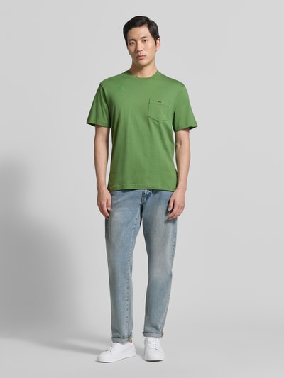 Męski model nosi Regular Fit T-Shirt aus reiner Baumwolle von Lacoste, jednokolorowy efekt, wyhaftowane logo, nadruk z logo, okrągły dekolt, bawełna, Ganzkörperansicht von vorne.