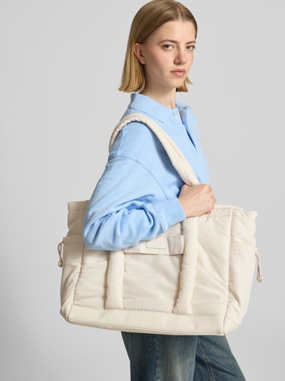 Frauenmodel trägt cremefarbene Handtasche mit Label-Patch Modell 'Cool Buddy' von Hey Marly, Hauptfach mit Reißverschluss, Tragehenkel, Breite 53 cm, Länge 35 cm, Tiefe 15 cm, Länge Schulterriemen 67 cm, Ganzkörperansicht von vorne