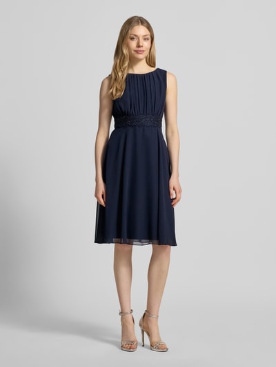 Frauenmodel trägt Knielanges Cocktailkleid mit Taillenband von Christian Berg Cocktail, dunkelblauer Chiffon, Drapierungen, taillierter Schnitt, Rundhalsausschnitt, Knielänge, Ganzkörperansicht von vorne. Rückenlänge bei Größe 36: 103 cm, Brustweite bei Größe 36: 36 cm.