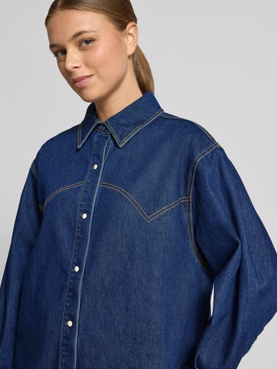 Kobiece model prezentuje Relaxed Fit Jeansbluse mit Knopfleiste od Scotch & Soda, mieszanka bawełny z dodatkiem streczu, kołnierzyk koszulowy, listwa guzikowa, ciemnoniebieska tkanina o gładkiej fakturze, długość tyłu 56 cm, długość rękawów 73 cm, rozmiar 36, zbliżenie na górną część sylwetki, widok z przodu.