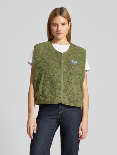 Vrouwenmodel draagt bodywarmer met ronde hals Model 'HOKTOWN' van American Vintage, teddybont, steekzakken, labeldetail, los model, drukknoopsluiting, kleur olijfgroen, voorkant volledige lichaamsopname.