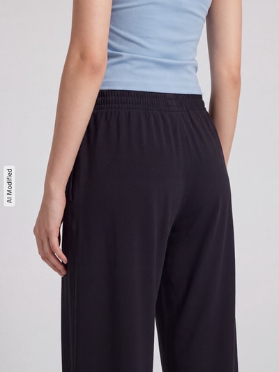Frauenmodel trägt Wide Leg Sweathose mit Logo-Print von Under Armour in Dunkelblau, glatte Struktur, Ganzkörperansicht Rückansicht, KI-modifiziertes Bild.