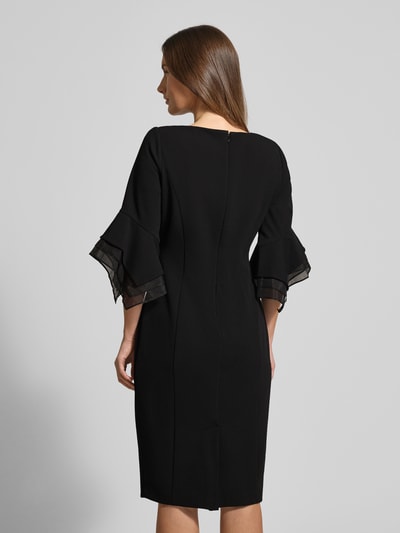 Frauenmodel trägt knielanges Cocktailkleid mit Trompetenärmeln von Adrianna Papell, Material-Mix mit Stretch-Anteil, gerader Schnitt, schwarze Farbe, Rückenlänge 102 cm, Ganzkörperansicht Rückansicht.