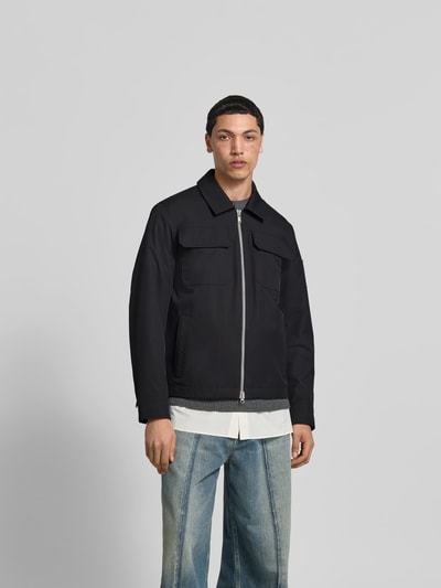 Männermodel trägt Jacke mit Umlegekragen von Moose Knuckles in Schwarz, Gerade Passform, Brusttaschen, Zweiwege-Reißverschluss, Label-Patch, Ganzkörperansicht von vorne, Rückenlänge bei Größe M 67 cm, Schulterbreite 47 cm, Ärmellänge 66 cm.