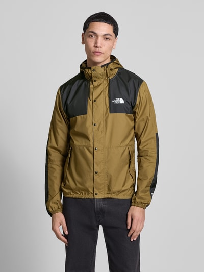 Mannelijk model draagt heren jack met regular fit, logoprint, capuchon met tunnelkoord, steekzakken met ritssluiting, elastische boorden, model 'Mountain' van The North Face, kleur groen en zwart, gladde textuur. Ganzkörperansicht von vorne.