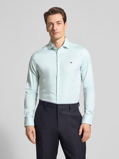 Männermodel trägt 'Slim Fit Freizeithemd aus Baumwoll-Mix' von Tommy Hilfiger, kolor melanż, krój slim fit, kołnierzyk typu kent, długi rękaw, listwa guzikowa, detal z logo, pas na plecach, zakończenie zaokrąglone, wykończenie materiału: popelina, mieszanka bawełny, Ganzkörperansicht von vorne.