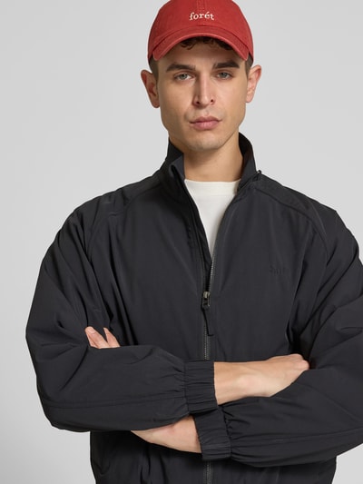 Männermodel trägt Basecap mit Label-Stitching von Forét in Rot im Denim-Look mit Steppnähte, verstellbarem Riegel, Nahaufnahme Oberkörper.