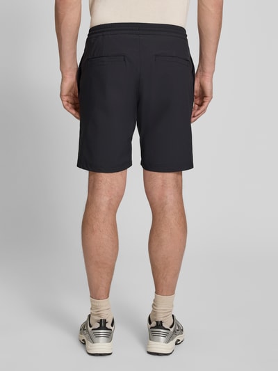 Męski model nosi Straight Fit Shorts mit Eingrifftaschen Modell 'Drift' von SCANDINAVIAN EDITION, czarny elastyczny materiał, kieszenie, prosty krój, elastyczny pas z troczkiem, widok z tyłu całej sylwetki.