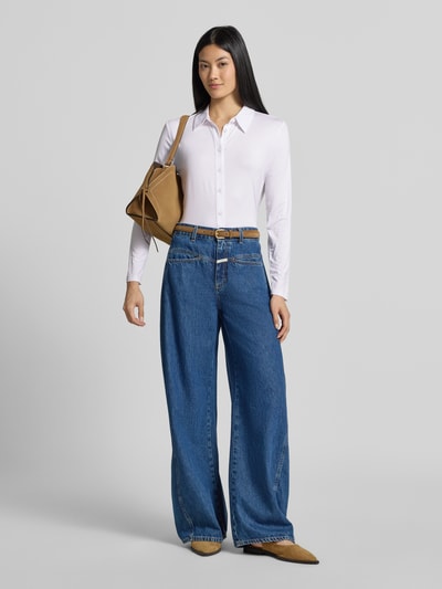 Frauenmodel trägt Slim Fit Hemdbluse aus Viskose-Mix von COMMA in Weiß, kombiniert mit blauer Jeans, glatte Stofftextur, Ganzkörperansicht von vorne, elastischer Viskose-Mix, Hemdblusenkragen, durchgehende Knopfleiste, langärmliges Design, Rückenlänge 55 cm, Ärmellänge 58 cm.