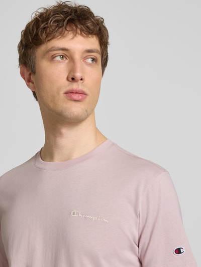 Männermodel trägt T-Shirt mit Label-Stitchings und Rundhalsausschnitt von CHAMPION in Rosa, reine Baumwolle, Nahaufnahme Oberkörper.
