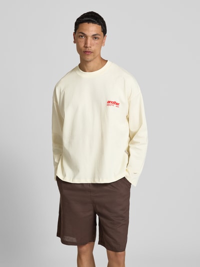 Męski model nosi bluzkę z długim rękawem z nadrukiem z logo i okrągłym dekoltem od ANOTHER COTTON LAB, bawełna, krój relaxed fit, długość tyłu w rozmiarze M: 65 cm, widok całej sylwetki z przodu.