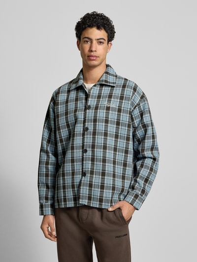 Männermodel trägt Regular Fit Freizeithemd mit Label-Stitching von Pegador, Modell 'Rupit', kariert in Blau und Braun, Kentkragen, Knopfleiste, Rückenlänge 72 cm, Schulterbreite 59 cm, Ärmellänge 61 cm, Ganzkörperansicht von vorne.