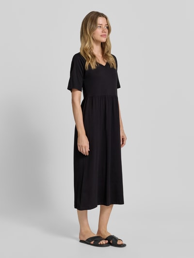 Frauenmodel trägt Damen Midikleid mit Smok-Detail Modell 'DERBY' von Soyaconcept, schwarze Reine Baumwolle, A-Linie, Ganzkörperansicht von vorne. Kontext: Rückenlänge bei Größe S 117 cm, Brustweite 44 cm, Ärmellänge 27 cm, Rundhalsausschnitt.