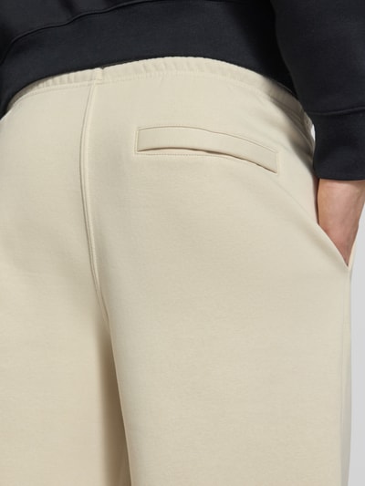 Männermodel trägt Sweatpants mit Logo-Stitching und Eingrifftaschen von Nike aus Baumwoll-Mix in Beige, Detailaufnahme Gesäßtasche.