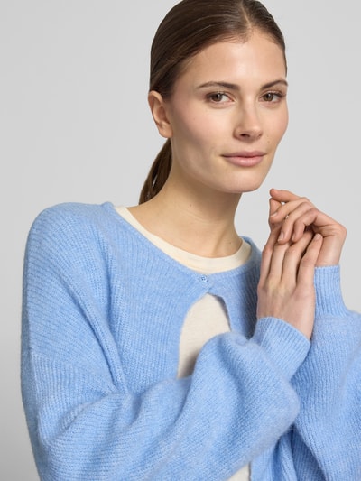 Modelka nosi jasnoniebieski kardigan z mieszanki materiałów z dodatkiem wełny, model 'Deriana' od OPUS, zapięcie na guzik, tekstura miękka, długość tyłu 51 cm, długość rękawów 58 cm, widok z przodu, zbliżenie na górną część ciała.