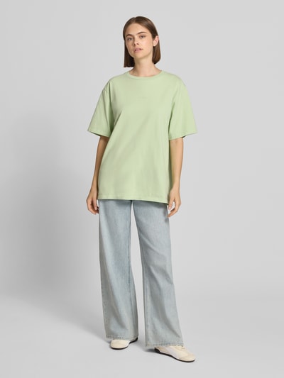 Frauenmodel trägt Oversized T-Shirt mit rückseitigem Print Modell 'Midsummer' von OH APRIL in Hellgrün, reine Baumwolle, Ganzkörperansicht von vorne.